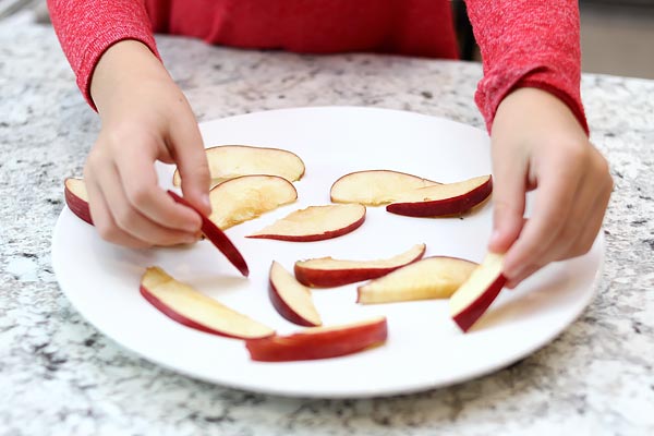 Child spreading apple slices on a plate