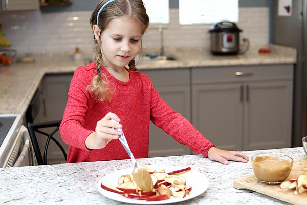 Girl spreading peanut butter on apples
