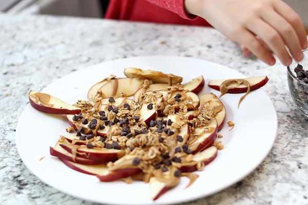 Preschooler adding chocolate chips onto apple slices