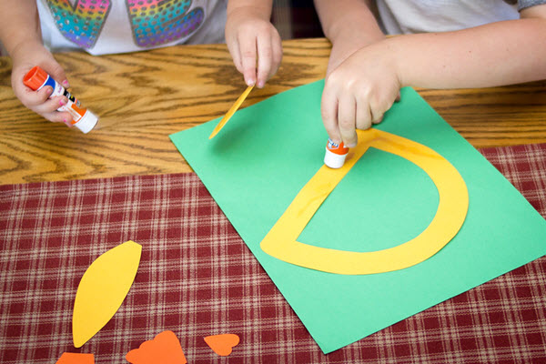 child gluing the letter d