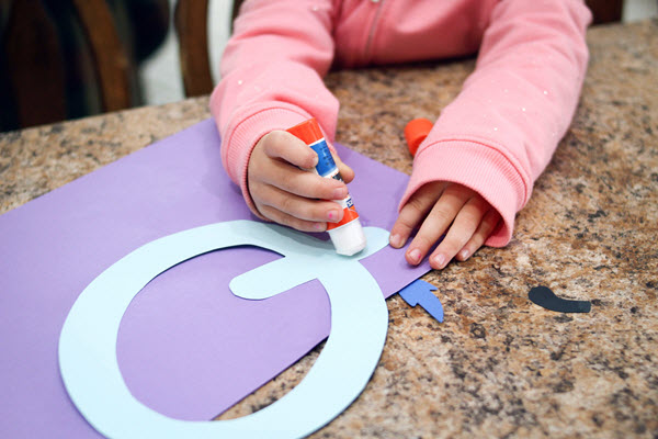 little girl gluing the letter q for her letter q craft