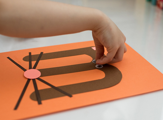 child attaches googly eye to uppercase m craft