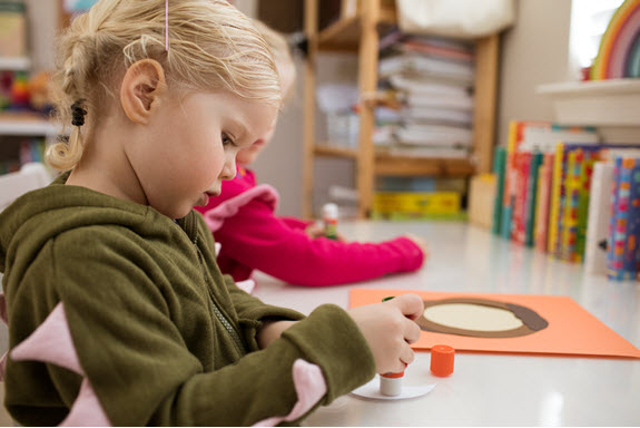 child puts glue on her uppercase letter O craft