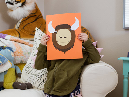 child hides behind her uppercase letter O craft