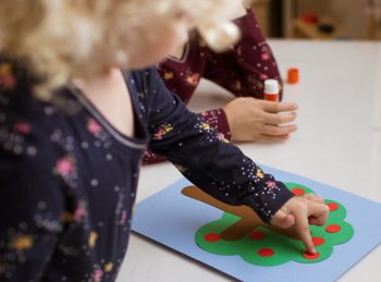 child affixes an apple to her lowercase T craft