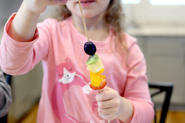 girl creating rainbow fruit skewers
